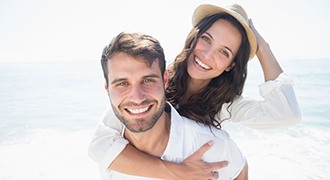 young couple smiling on beach with veneers in Tyler