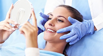 young woman sitting in dental chair and smiling at hand mirror 
