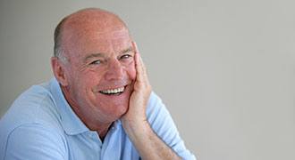 Older bald man in blue shirt smiling with his dentures