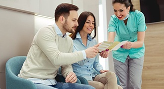 dental team member showing a pamphlet to two patients 