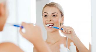 Woman brushing teeth to prevent dental emergencies in Tyler