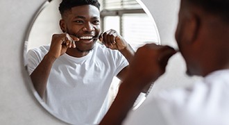 Man smiling while flossing his teeth in mirror