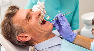 Older man being examined by Dr. Franklin-Pitts and hygienist