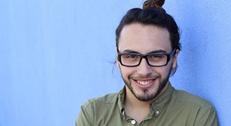 man with green shirt and hair in bun smiling in front of blue wall 