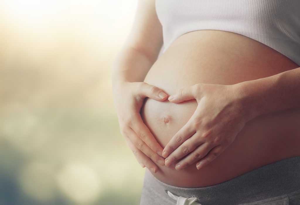 Woman with heart-shaped hands over pregnant belly