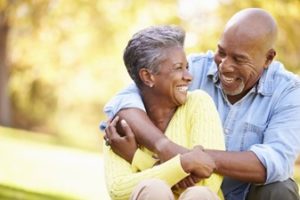 Man wearing a denim shirt and a woman wearing a yellow sweater cuddling and smiling